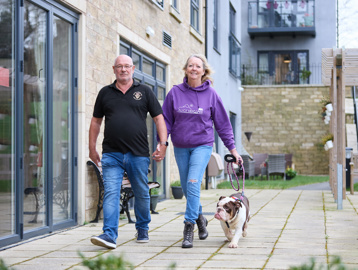 Extra Care residents Graham and Marlene walking their dog outside in communal garden area