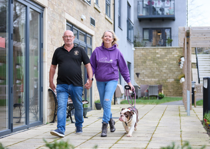 Extra Care residents Graham and Marlene walking their dog outside in communal garden area