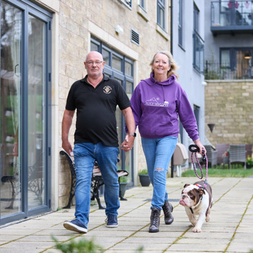 Extra Care residents Graham and Marlene walking their dog outside in communal garden area