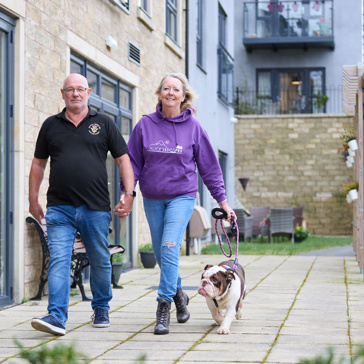 Extra Care residents Graham and Marlene walking their dog outside in communal garden area