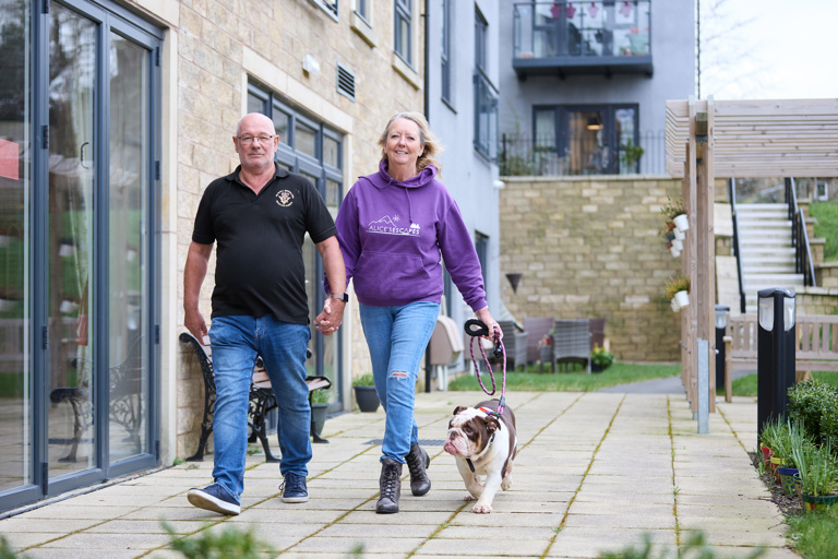 Extra Care residents Graham and Marlene walking their dog outside in communal garden area