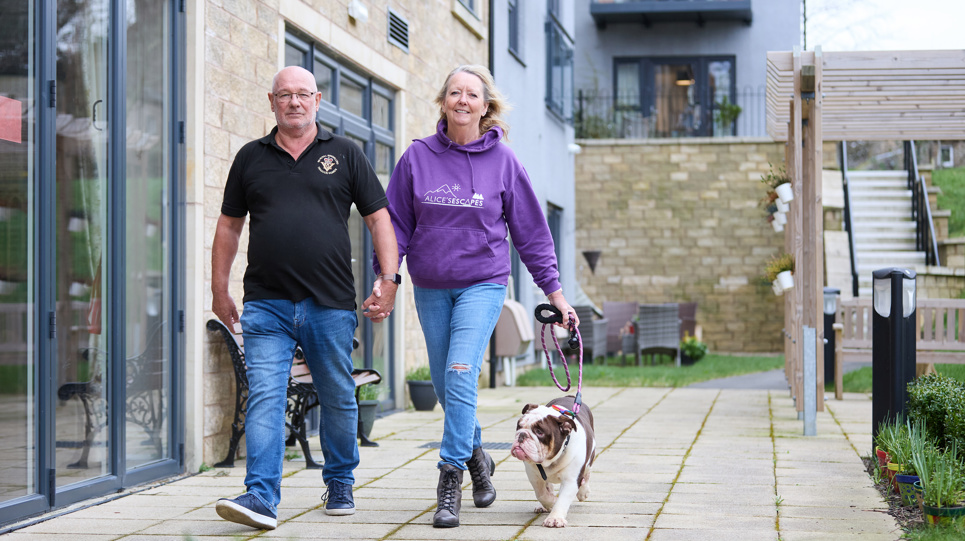 Extra Care residents Graham and Marlene walking their dog outside in communal garden area