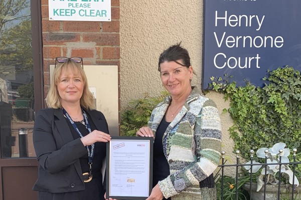 Two women hold a plaque outside Henry Vernone Court