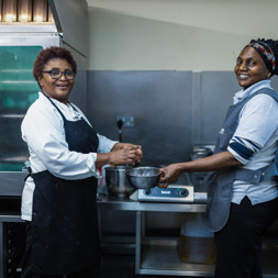 Two Housing 21 employees wearing aprons in a kitchen looking to camera and smiling