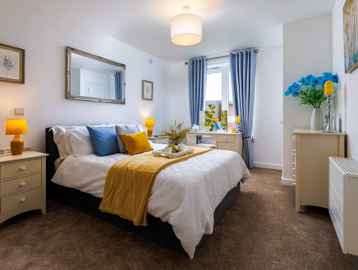A photo of the master bedroom in the show apartment with double bed and soft furnishings in blue and yellow