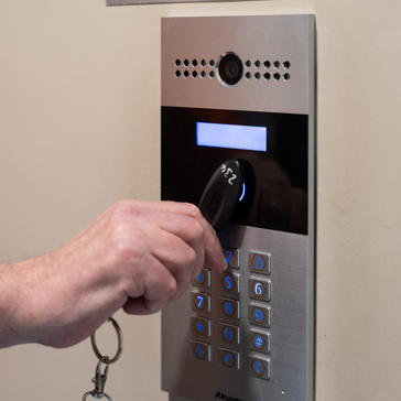 A hand clutching an access fob swipes the door entry control panel