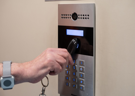 A hand clutching an access fob swipes the door entry control panel