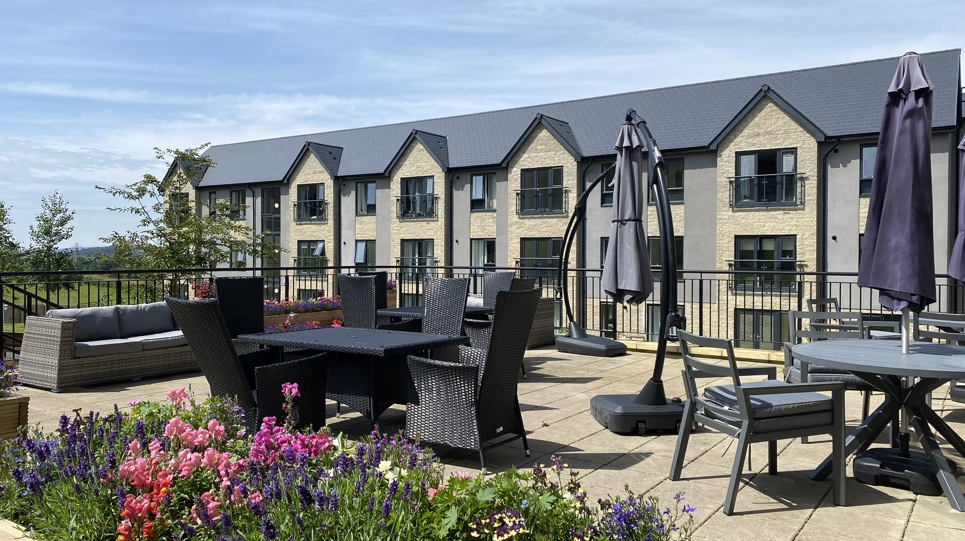 A seating area in the gardens of Castlestead View with tables, chairs and plants overlooked by the building and balconies
