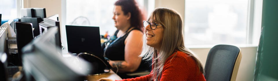 Corporate employees smiling sitting at their desk in front of a computer  