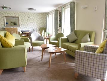 Resident's lounge area with soft armchair and sofa seating with tables