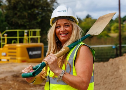 A smiling woman in a hard hat with a shovel