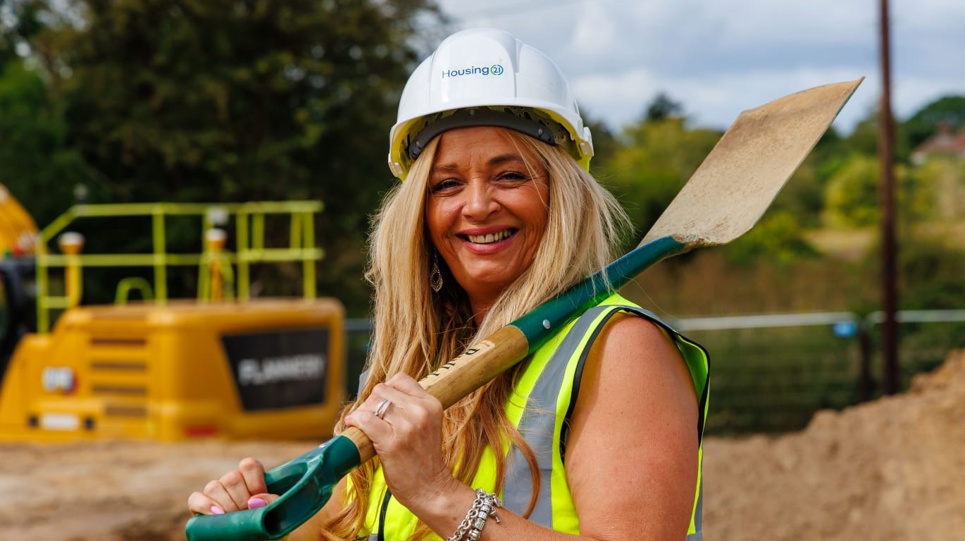 A smiling woman in a hard hat with a shovel