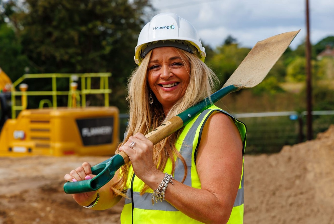 A smiling woman in a hard hat with a shovel