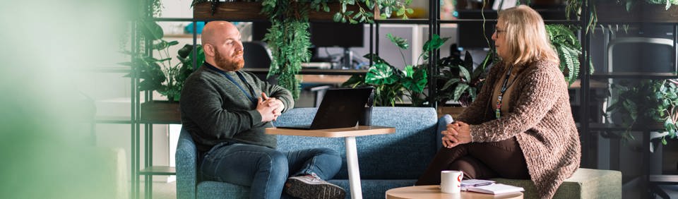 Two employees sat around a table with a laptop talking