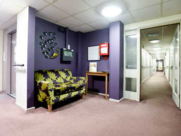 Communal hallway with floral pattern sofa and carpeted areas leading to apartments