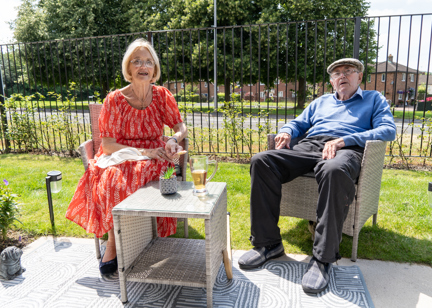 A Housing 21 couple sat outside their apartment enjoying a drink on their patio on a sunny day