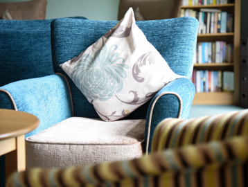 Close-up of a floral cushion on a blue and cream armchair in the communal lounge