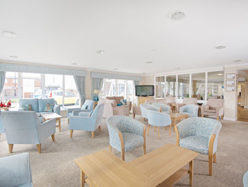 Residents' communal lounge with soft seating and tables in light blue colour scheme