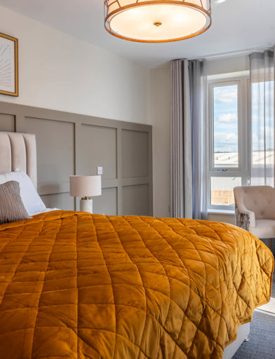 Inside the show home apartment master bedroom with double bed, chairs and coffee table 