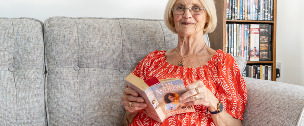 Resident in a red dress sat on a sofa in their apartment reading a book