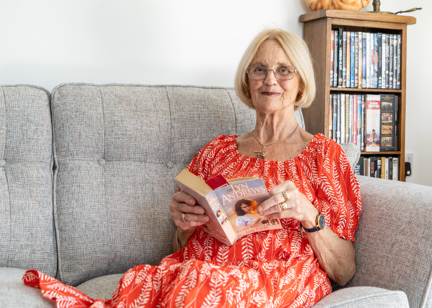 Resident in a red dress sat on a sofa in their apartment reading a book