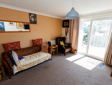 Bright living room with leather sofa, cushions and artwork, featuring sliding doors that lead to the garden