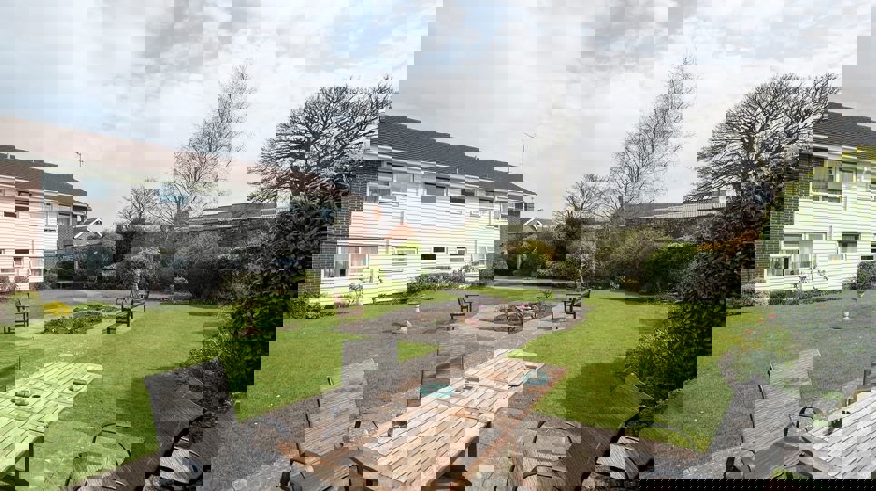 Garden to the rear of the scheme with a table and chairs, and trees and plans around the lawn area