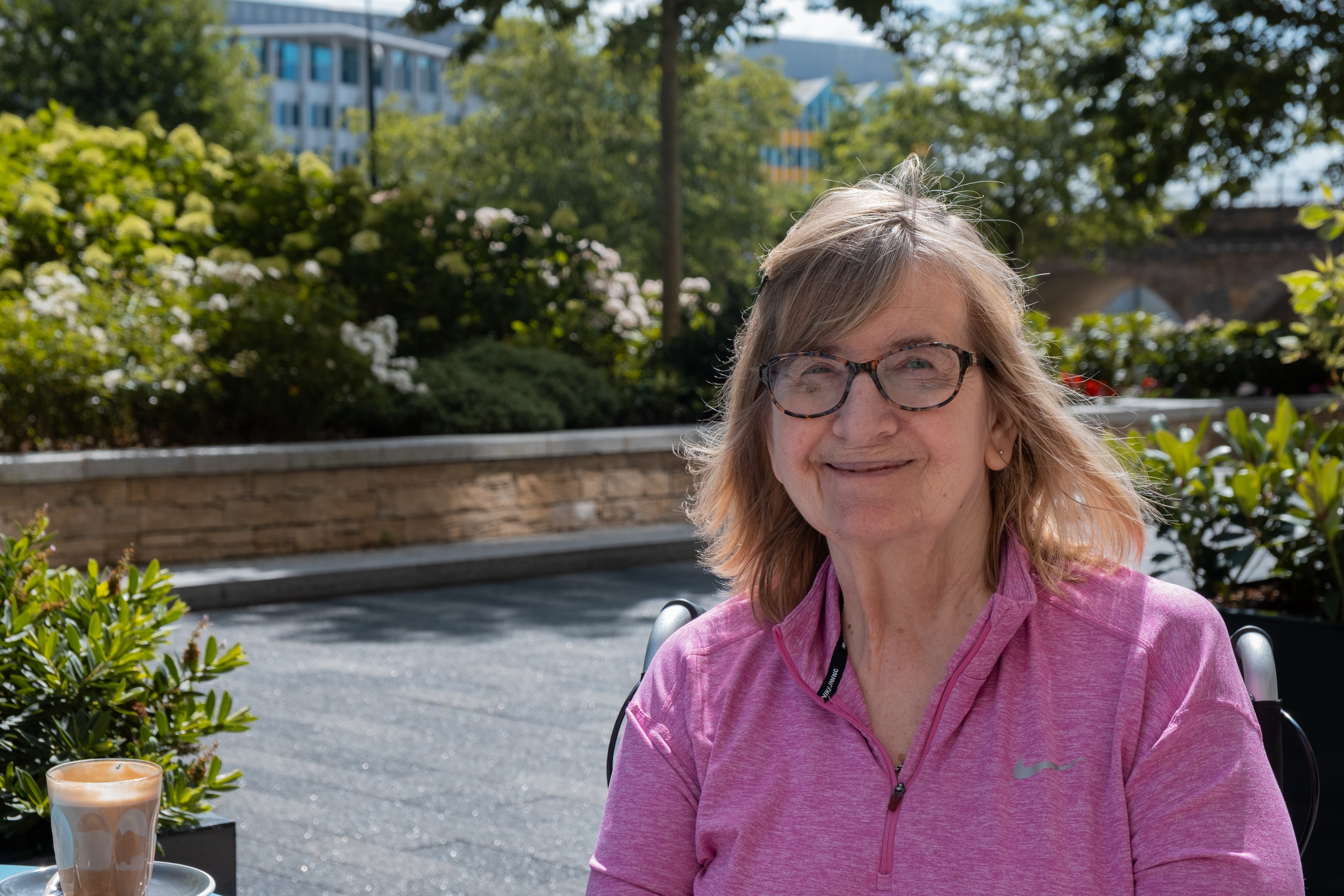 Resident Janet smiling sitting in the garden in a wheelchair wearing a pink sports jacket