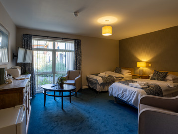 Guest room at Oakwood Gardens. Featuring a twin bed room with a tv, arm chair and table 