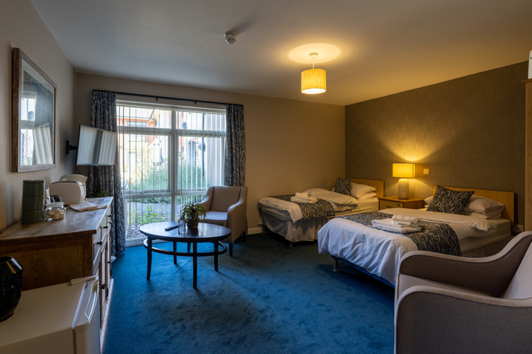 Guest room at Oakwood Gardens. Featuring a twin bed room with a tv, arm chair and table 
