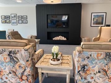 Showing the communal lounge at Michaelmas Court. Featuring a flat screen tv on the wall with a range of arm chairs facing the tv screen