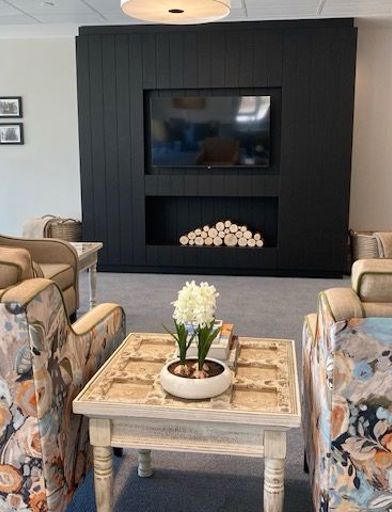 Showing the communal lounge at Michaelmas Court. Featuring a flat screen tv on the wall with a range of arm chairs facing the tv screen 