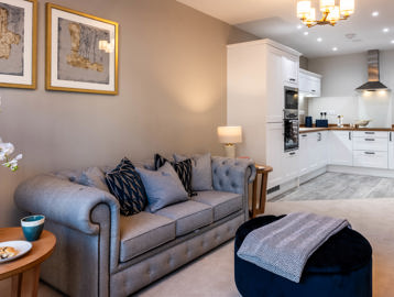 Inside the show home living area with large sofa and kitchen