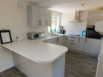A white kitchen on brown wooden flooring featuring an island breakfast table 