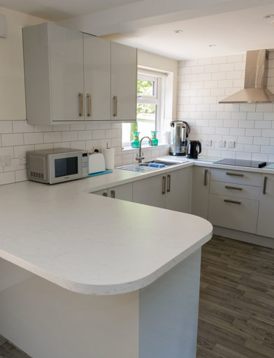A white kitchen on brown wooden flooring featuring an island breakfast table  