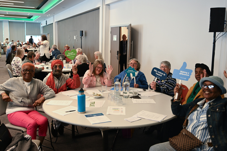 A table group shot of seven residents around a table all smiling and waving