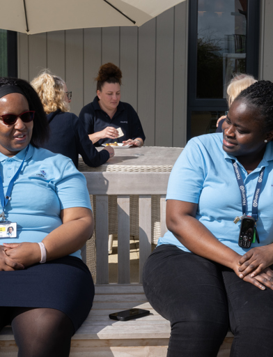Two colleagues in blue uniforms, enjoying the sun on a bench outside the scheme 