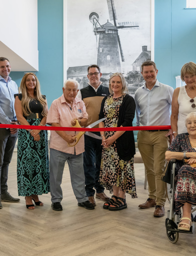 Housing 21 resident Arnold cuts the ribbon at an open day at Green View surrounded by Housing 21 colleagues and residents  