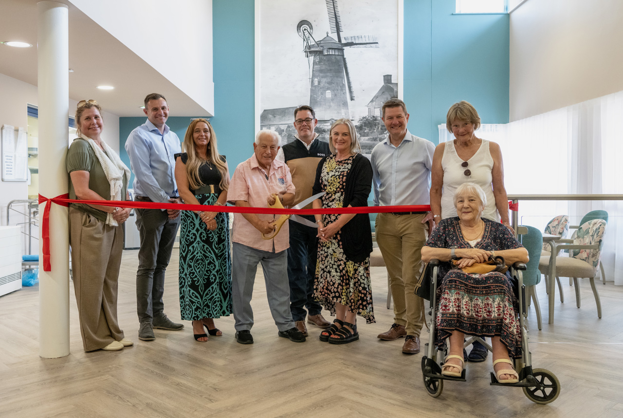 Housing 21 resident Arnold cuts the ribbon at an open day at Green View surrounded by Housing 21 colleagues and residents 