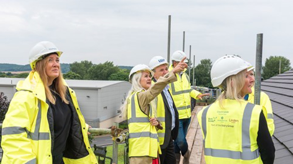 Housing 21 employees and stakeholders wearing high vis gather at the site of the Aldaniti Court development