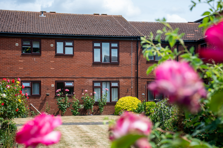 Exterior of building with dark brick work and roses in the garden