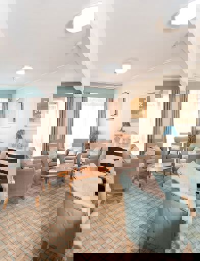 Residents' lounge with soft seating and coffee tables and check-patterned carpet 