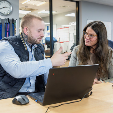 Two Housing 21 employees chat over a laptop whilst working at an Extra Care scheme