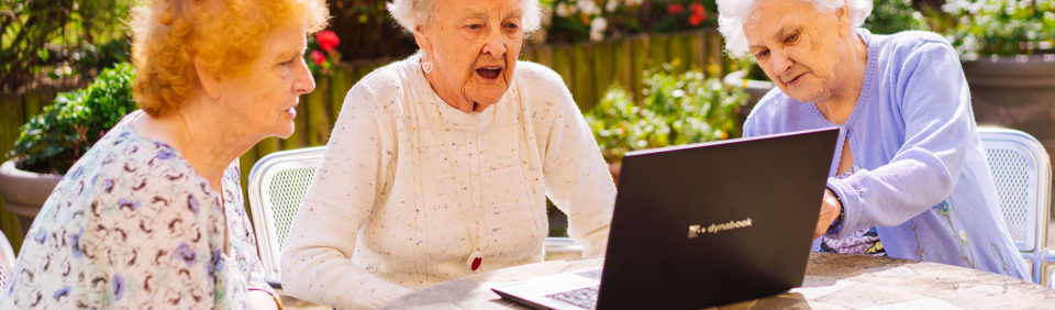 Three ladies gather around a laptop whilst sitting in a garden  