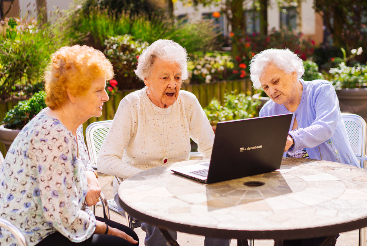 Three ladies gather around a laptop whilst sitting in a garden 
