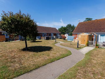 Shared green space with tree and private fenced gardens for each property, including washing lines and sheds.