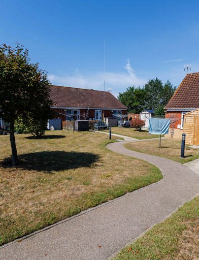 Shared green space with tree and private fenced gardens for each property, including washing lines and sheds.