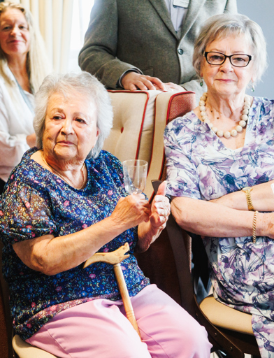 Two ladies in colourful tops, drink and smile to the camera 