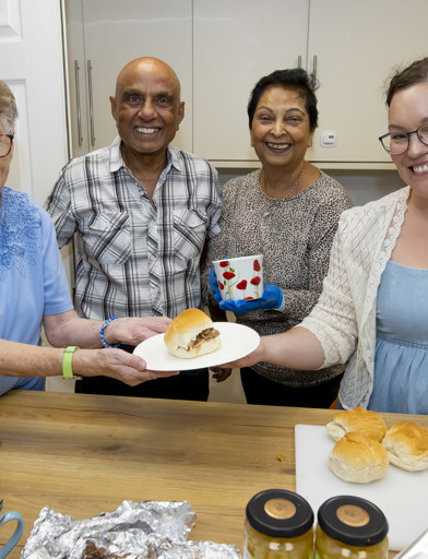 Three residents and a Housing 21 colleague in a kitchen area smiling holding a sandwich and tea 
