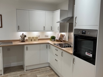 A kitchen with wooden flooring, white cupboards with an integrated oven and hob with wooden counter tops 